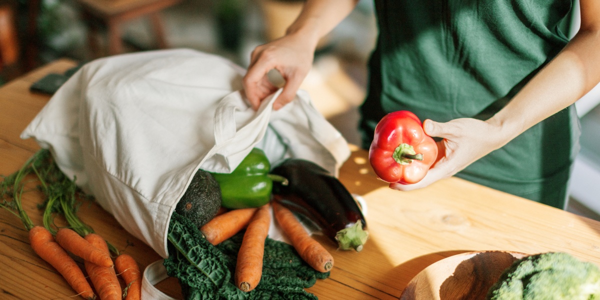 Eine Person packt Gemüse aus einer Stofftasche aus.