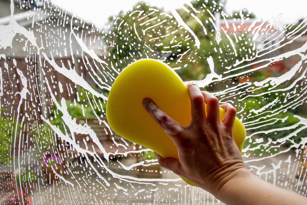 Jemand putzt mit einem Schwamm und Spülmittel eine Scheibe.