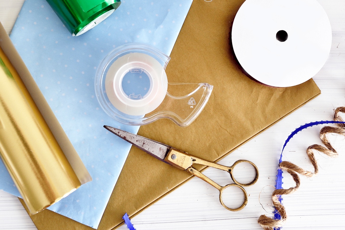 Geschenkverpackungszubehör mit Schere, Klebeband, Geschenkpapier und Dekoband.