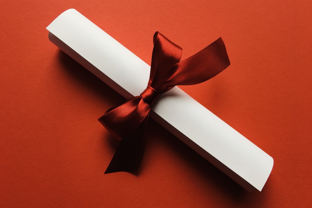 Gerolltes weißes Papier mit roter Schleife auf rotem Hintergrund.