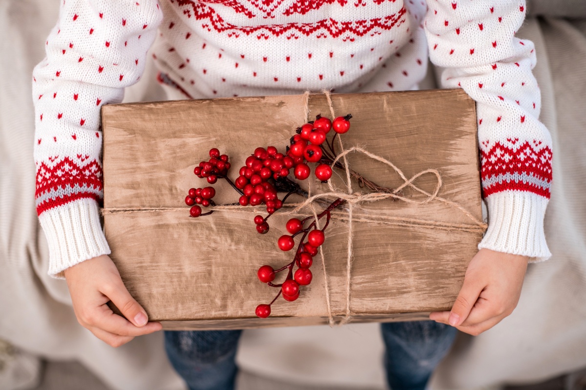 Kind hält Geschenk in braunem Papier mit Juteschnur und roten Beeren dekoriert.