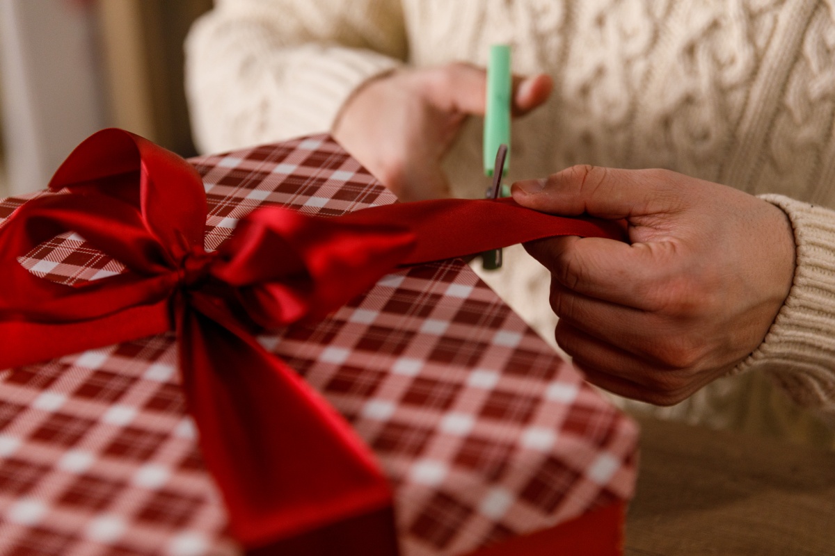 Person schneidet rote Schleife auf kariertem Geschenkpapier.