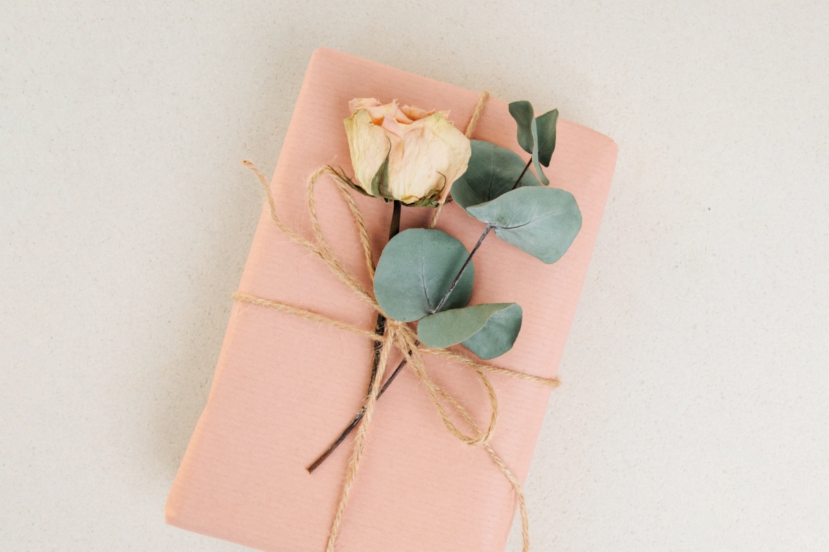 Geschenk in rosa Papier mit Juteschnur und getrockneter Rose verziert.