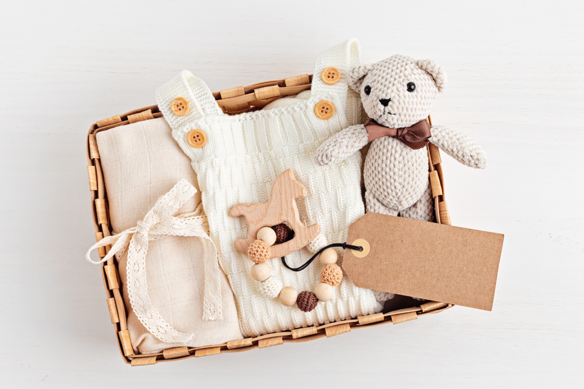 Geschenkkorb mit Babykleidung, Holzspielzeug und gehäkeltem Teddybär.