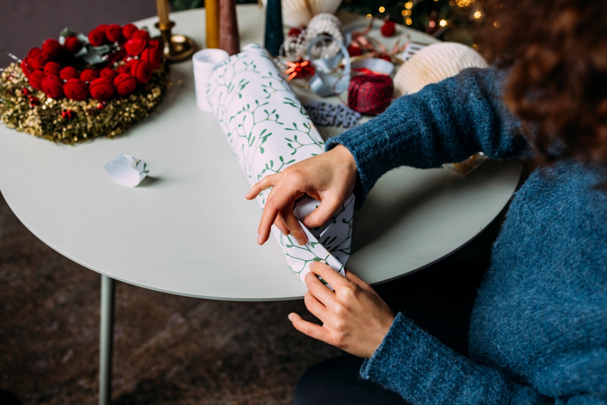 Person verpackt Geschenk in weiß-grünem Papier an einem festlich dekorierten Tisch.