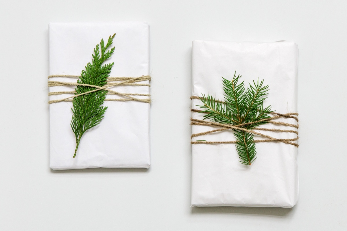 Zwei Geschenke in weißem Papier, dekoriert mit Juteschnur und grünen Zweigen.