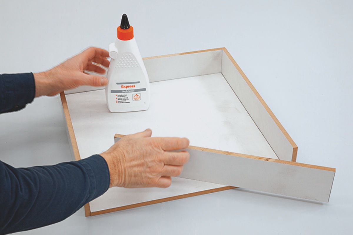 Arme einer Person, die aus fünf Holzfaserplatten eine Form verklebt. 