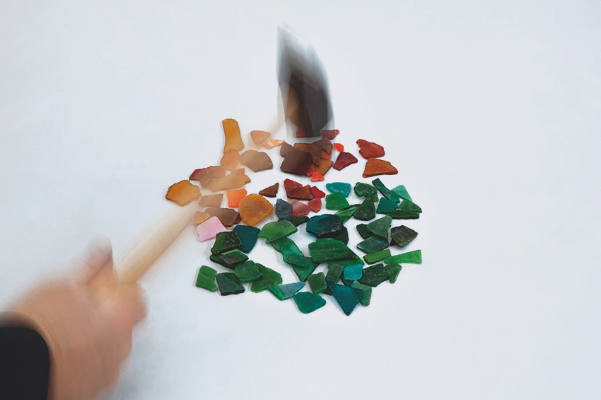 Person zerschlägt mit einem Hammer bunte Fliesen in kleine Teile.