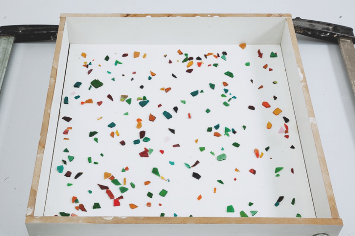 MDF-Form mit darauf drapiertem Fliesenbruch eingespannt zwischen zwei Schraubzwingen.