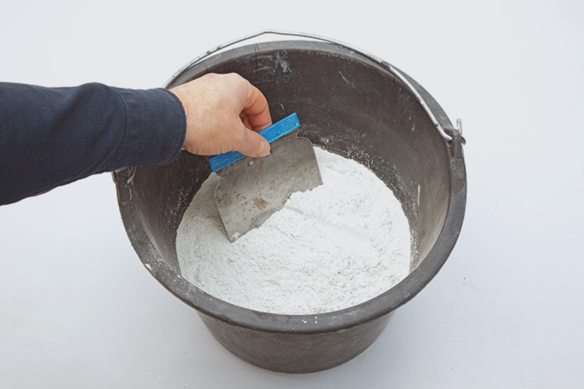 Eimer mit Sand-Zement-Mischung, eine Person verrührt diese mit einem Spachtel.