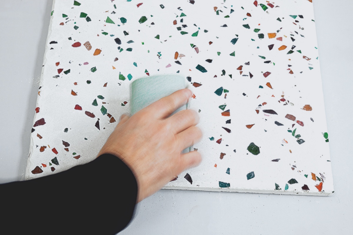 Person schleift Tischplatte in Terrazzo-Optik mit Sandpapier ab. 