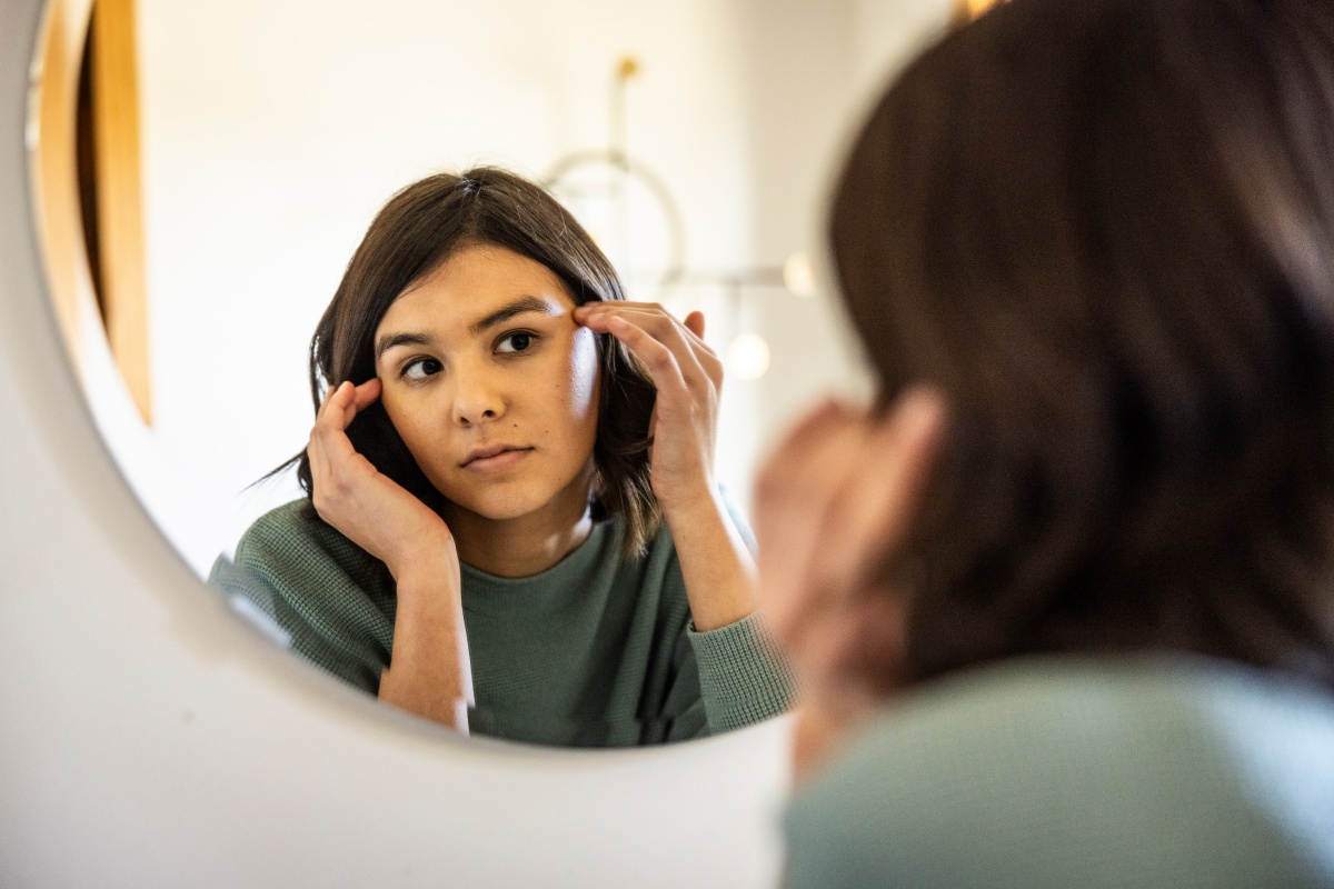 Frau betrachtet ihr Gesicht in einem runden Spiegel und überprüft ihre Haut.