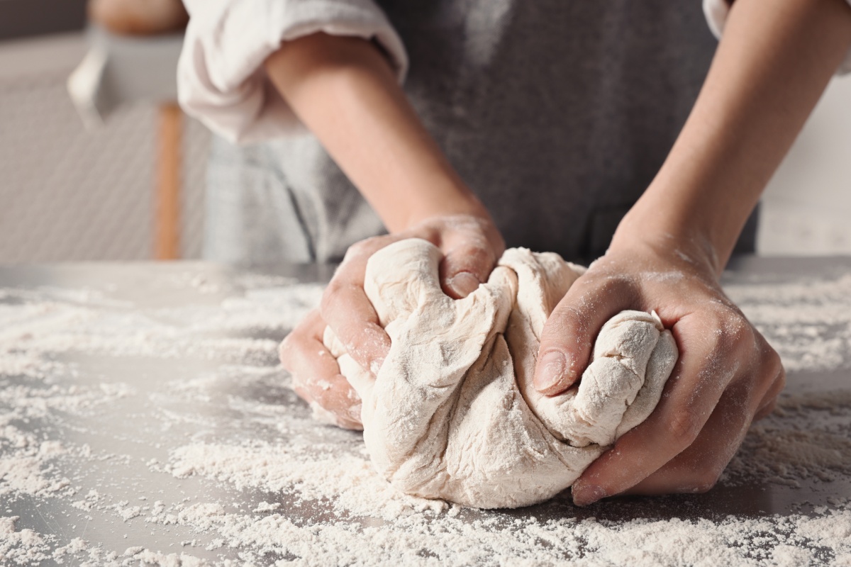 Jemand knetet Teig mit den Händen auf einer bemehlten Arbeitsfläche.