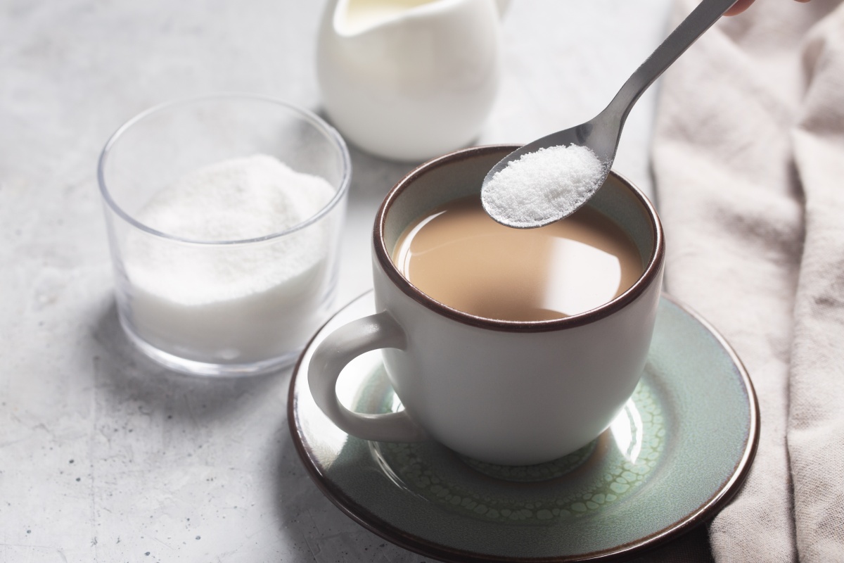 Jemand gibt weißen zuckerähnlichen Stoff Zucker mit einem Löffel in eine Tasse Kaffee.