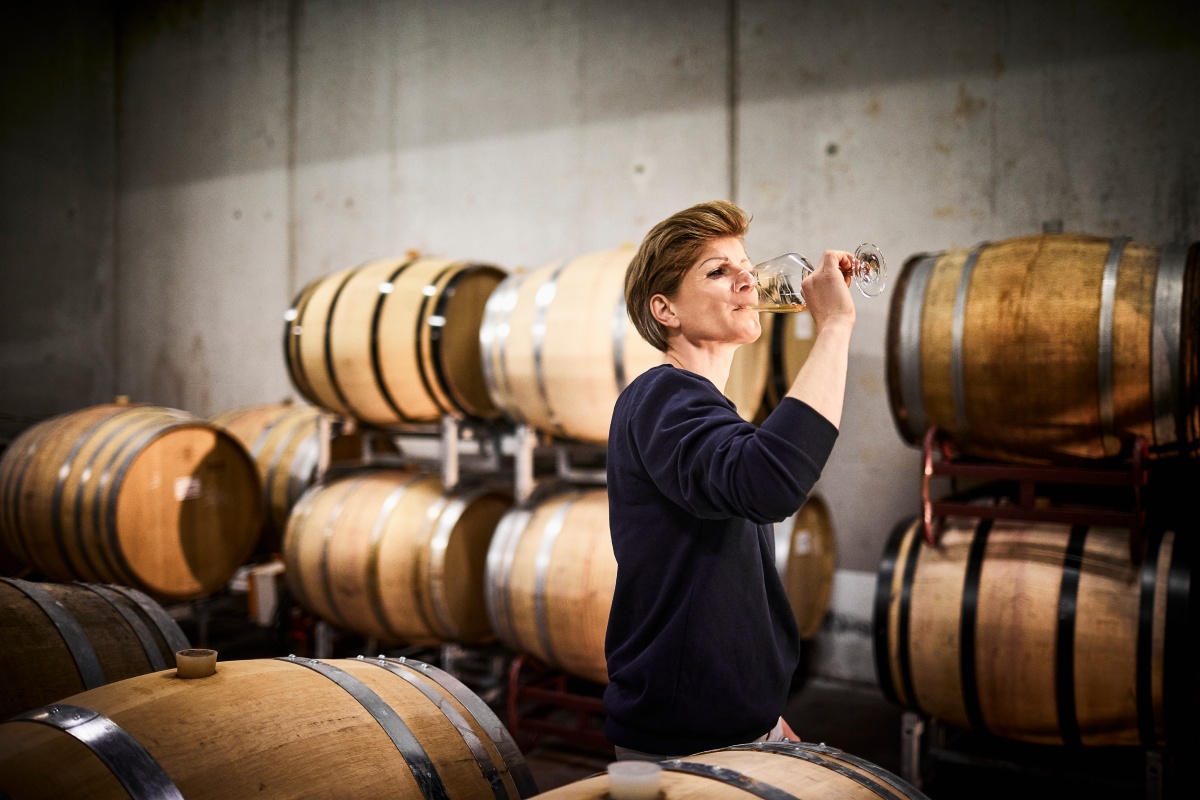 Die Winzerin probiert einen Cuvée Weißwein in der Kellerei, umgeben von Eichenfässern.
