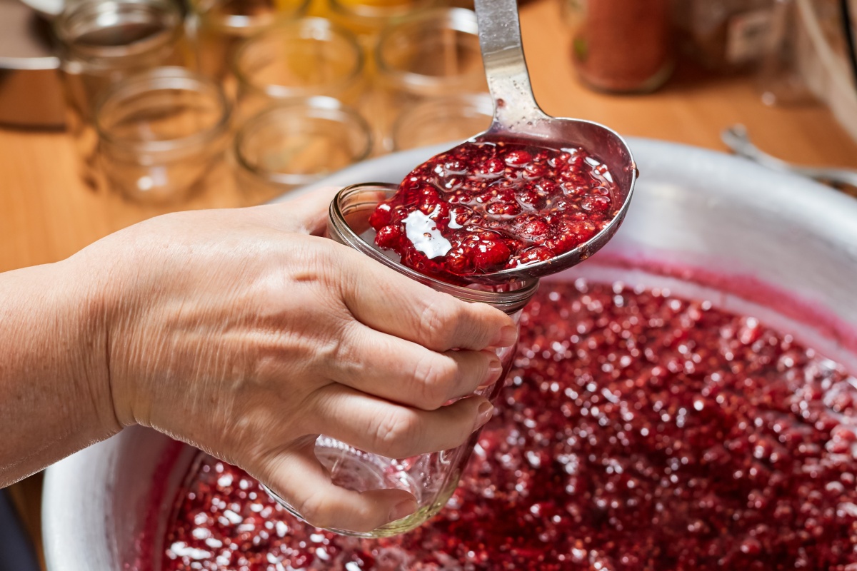 Jemand füllt frisch gekochte Himbeermarmelade in ein Glas zur Vorbereitung für das Einkochen im Backofen.