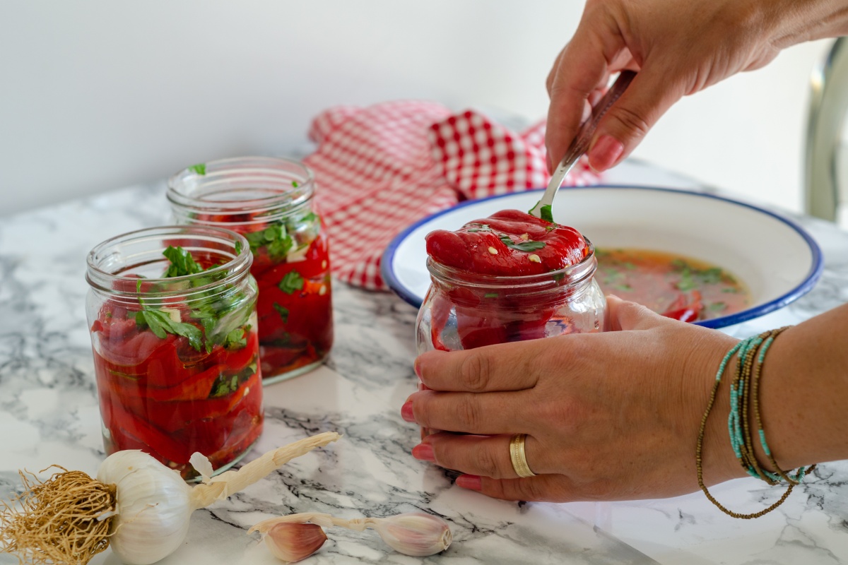 Person füllt marinierte Paprika mit Kräutern in ein Glas zur Vorbereitung für das Einkochen im Backofen.