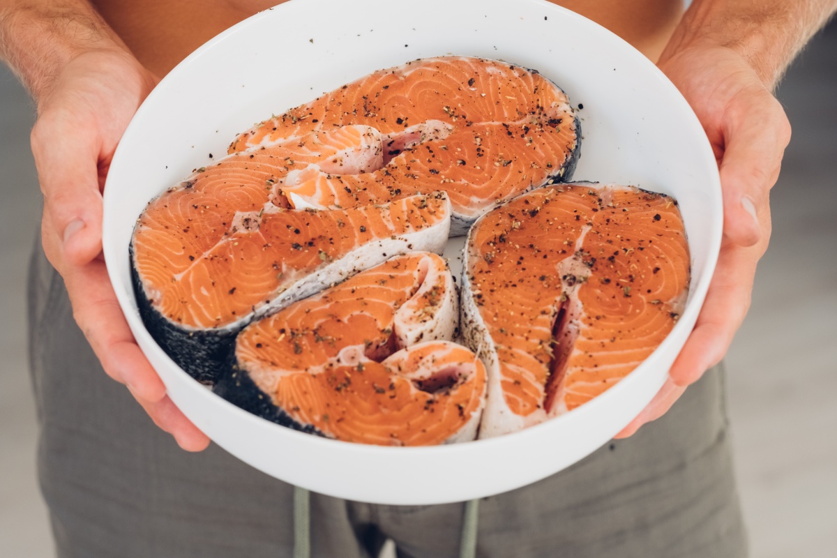 Eine Person hält eine Schale mit marinierten Fischfilets in den Händen.