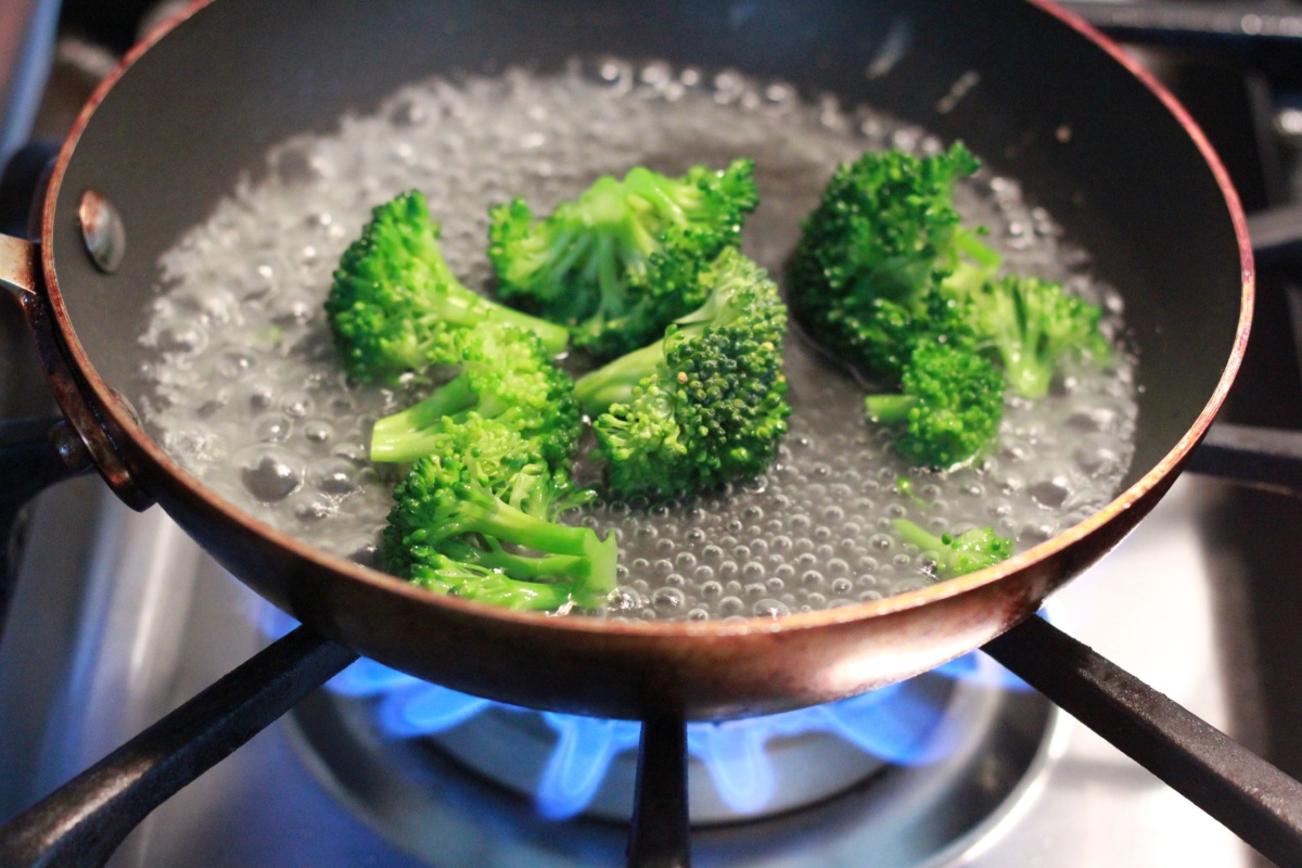 Brokkoliröschen dünsten in kochendem Wasser in einer Pfanne auf einem Gasherd.