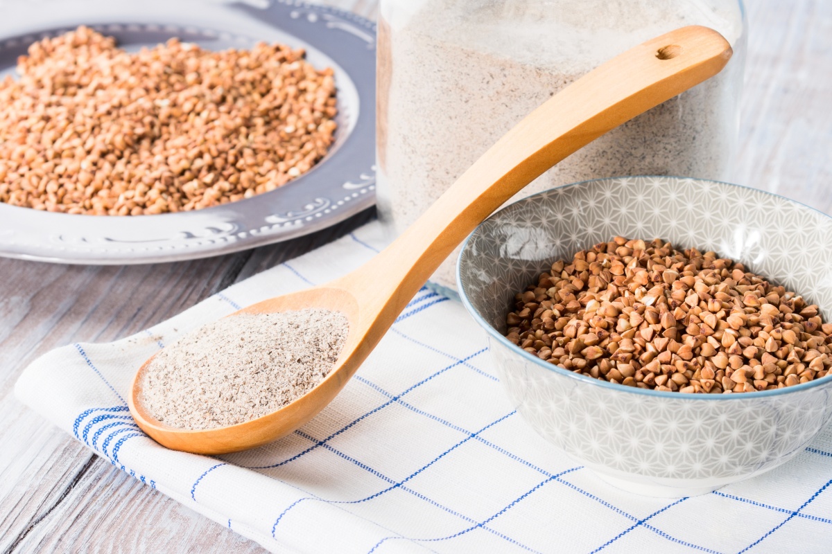 Ein Holzlöffel mit glutenfreiem Buchweizenmehl, daneben zwei Schalen mit Buchweizenkörnern.