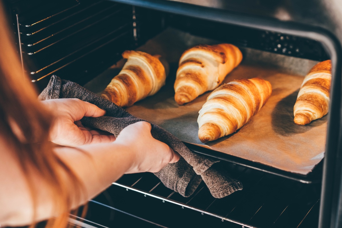 Eine Frau nimmt ein Blech mit frisch gebackenen Croissants aus dem Backofen.