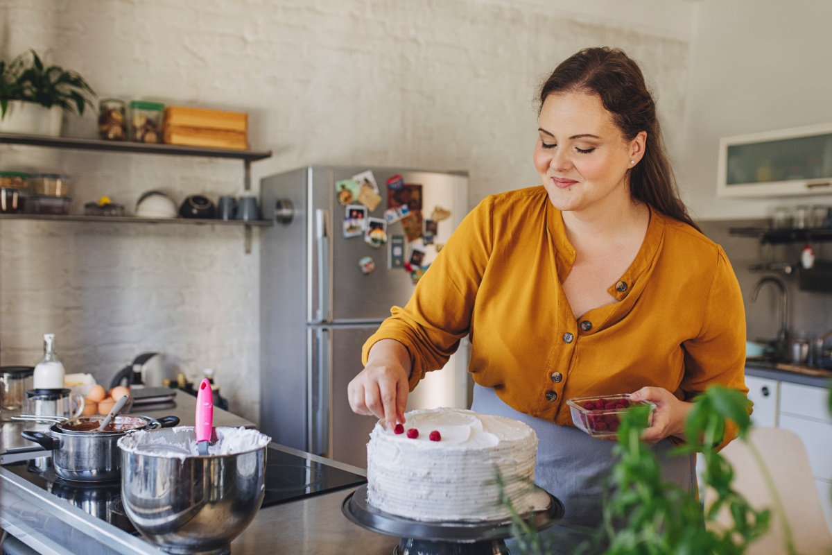 Frau verziert eine weiße Sahnetorte mit Himbeeren in der Küche.