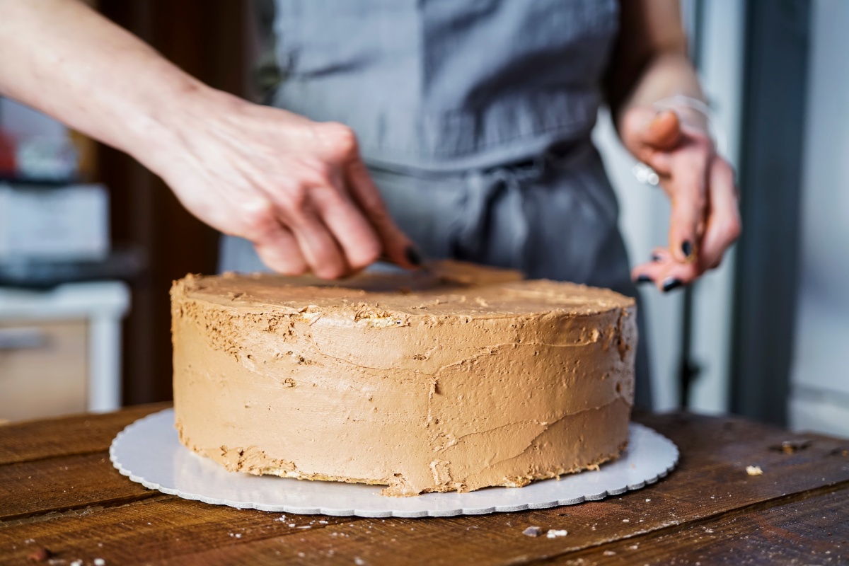 Jemand bestreicht runde Torte mit hellbrauner Schokoladencreme und glättet die Oberfläche für eine gleichmäßige Textur.