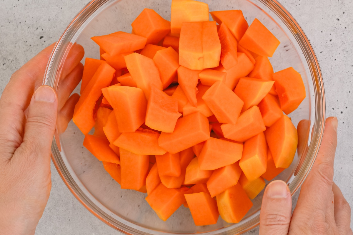 Hände halten eine Schüssel mit geschnittenen, orangen Kürbisstücken.
