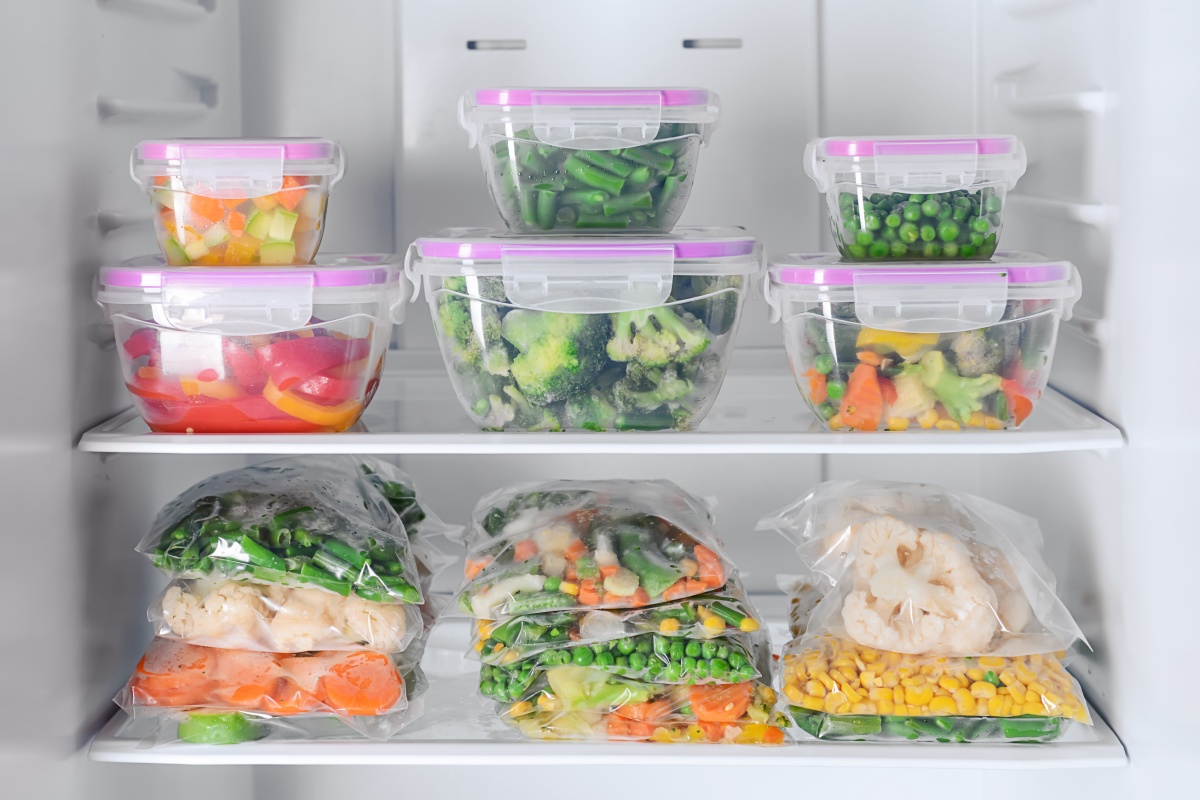 Gefrierfach mit  gemischtem, gefrorenem Gemüse wie Paprika, Brokkoli und Mais in Gefrierbeuteln und Plastikdosen verpackt.