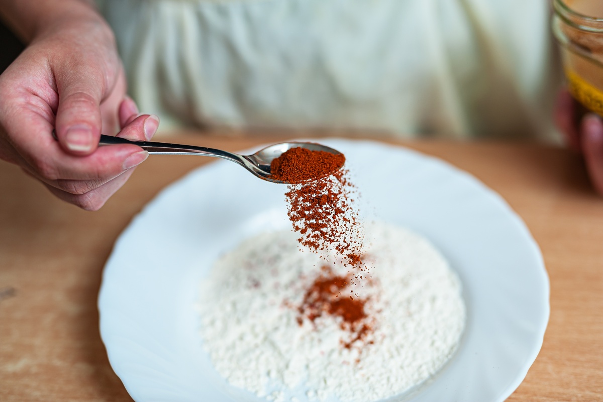Hand streut Paprikapulver aus einem Löffel in eine Schüssel mit Mehl.