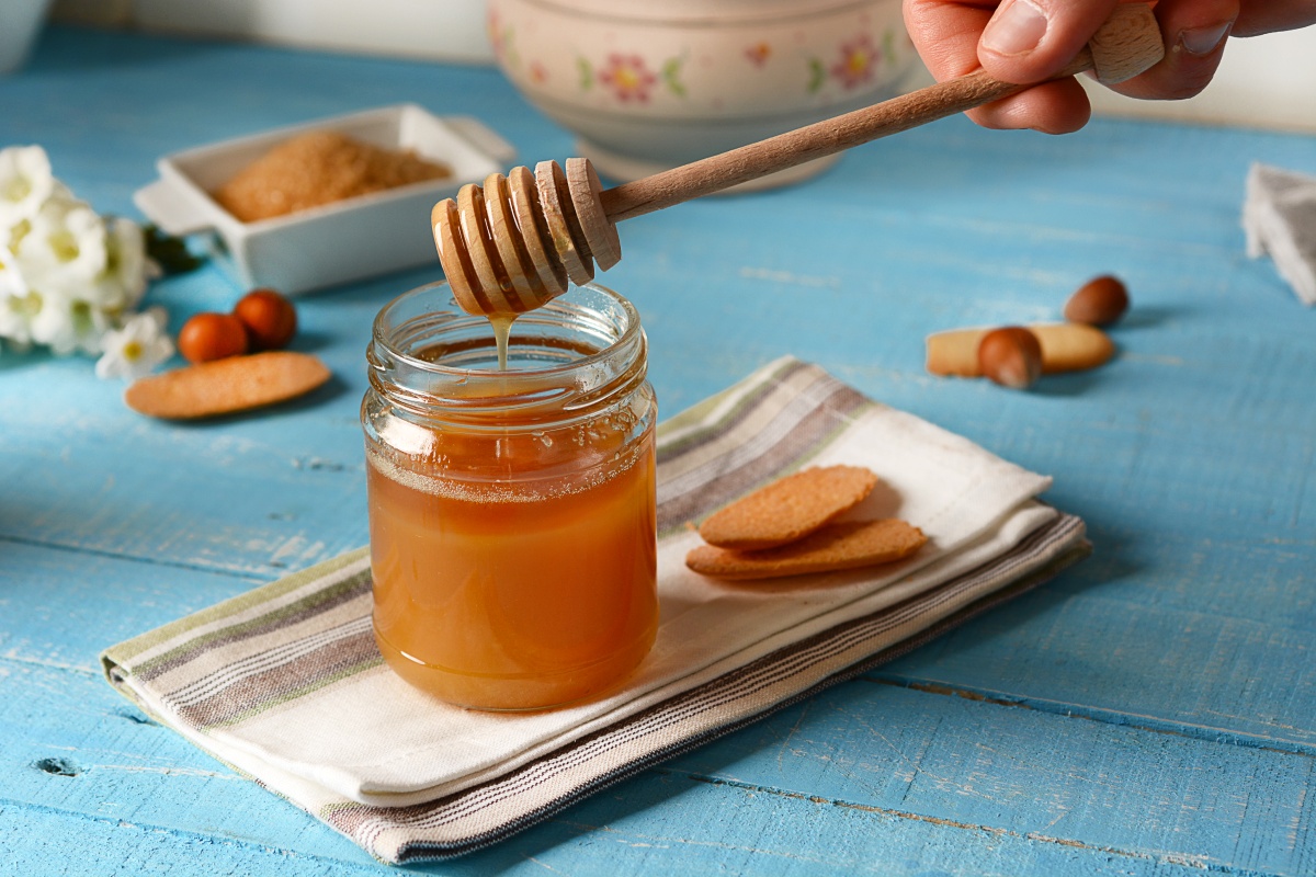 Glas mit flüssigem Honig und Holzlöffel. auf einem Tuch mit Keksen und Nüssen dekoriert.