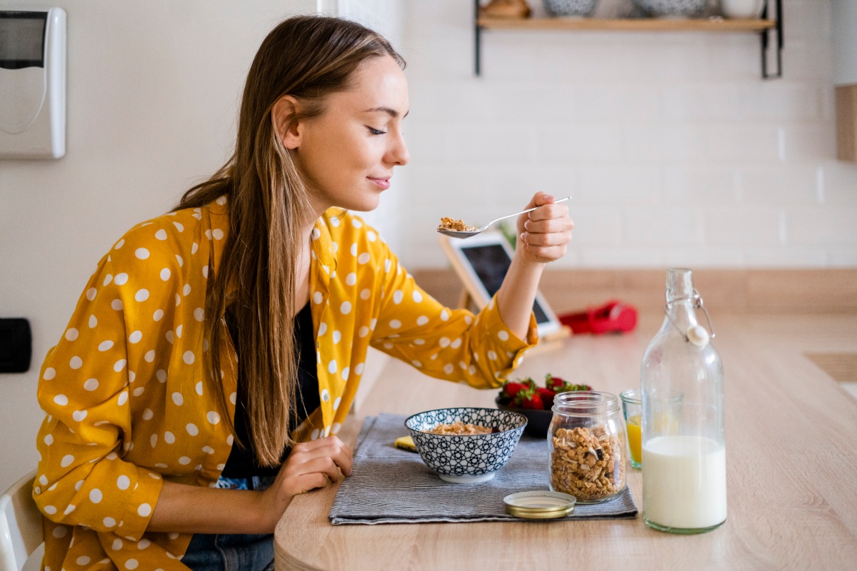 Frau in gelber gepunkteter Bluse genießt Müsli mit Milch zum Frühstück.