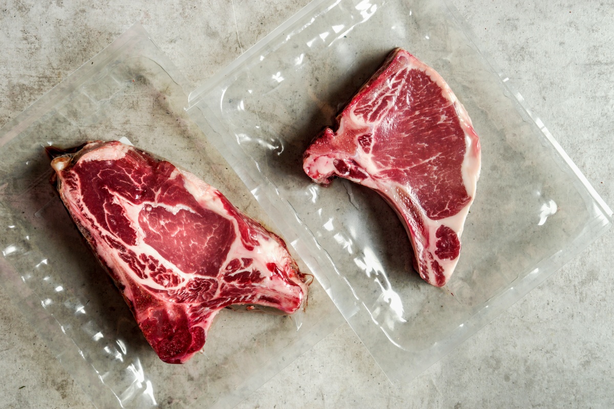 Zwei frische Fleischstücke in Vakuumverpackung auf grauer Oberfläche.