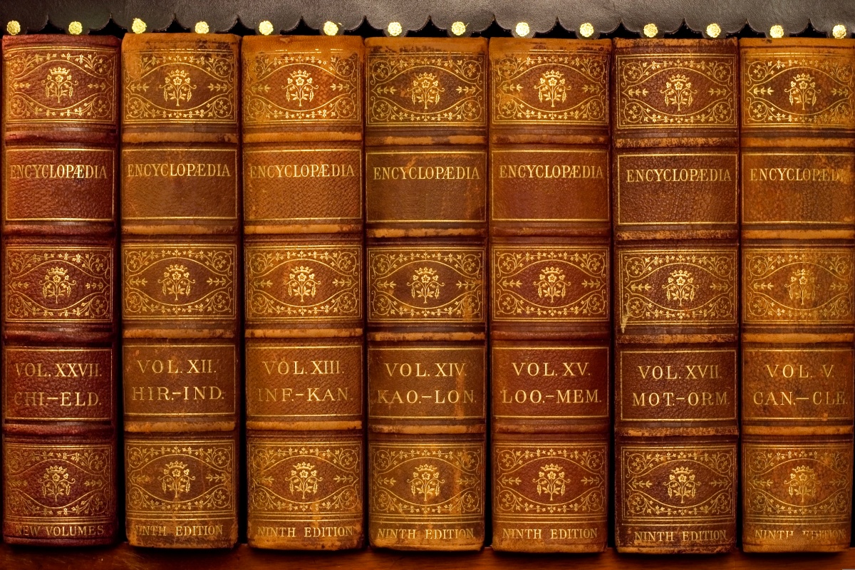 Nahaufnahme von alten, ledergebundenen Enzyklopädien in einem Regal, goldene Verzierungen auf den Buchrücken.