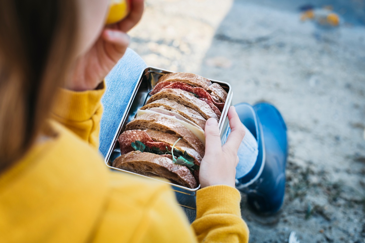 Ein sitzendes Kind hält eine Brotdose mit belegten Broten auf dem Schoß.