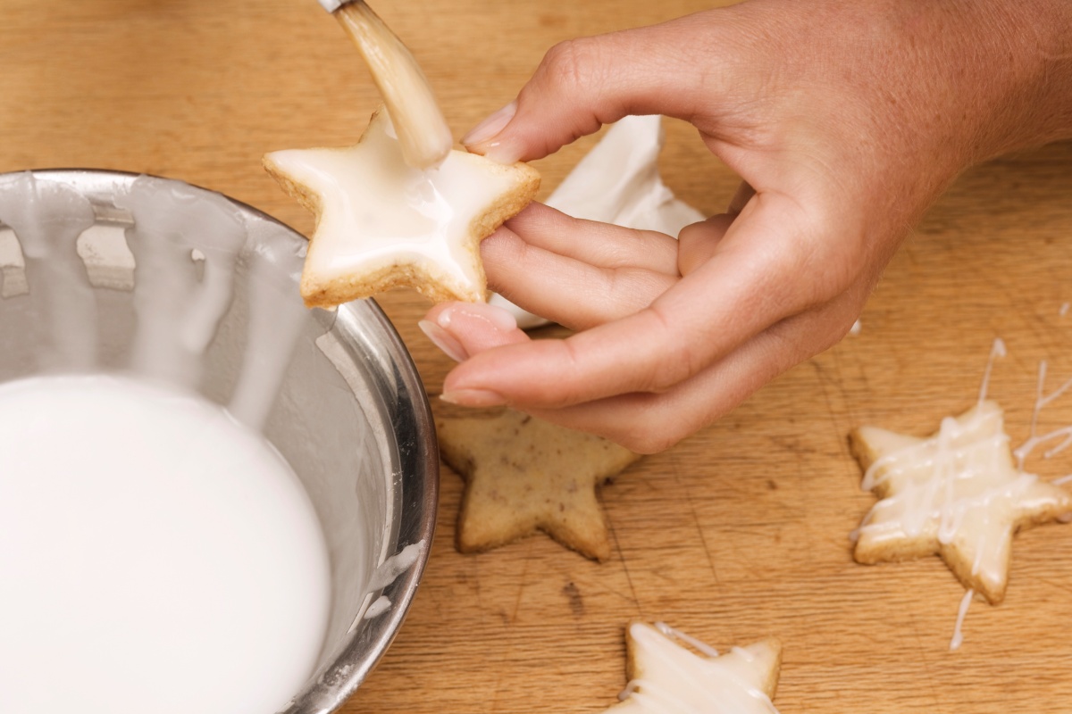 Jemand bestreicht ausgestochene sternförmige Plätzchen mit weißer Creme.