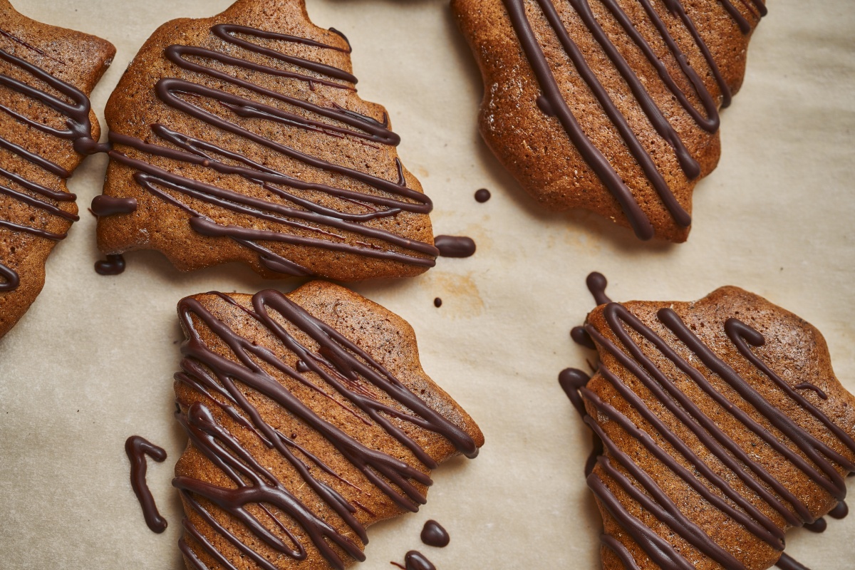 Tannenbaumförmige Lebkuchenplätzchen, dekoriert mit Schokoladenstreifen, auf Backpapier zum Abkühlen ausgelegt.