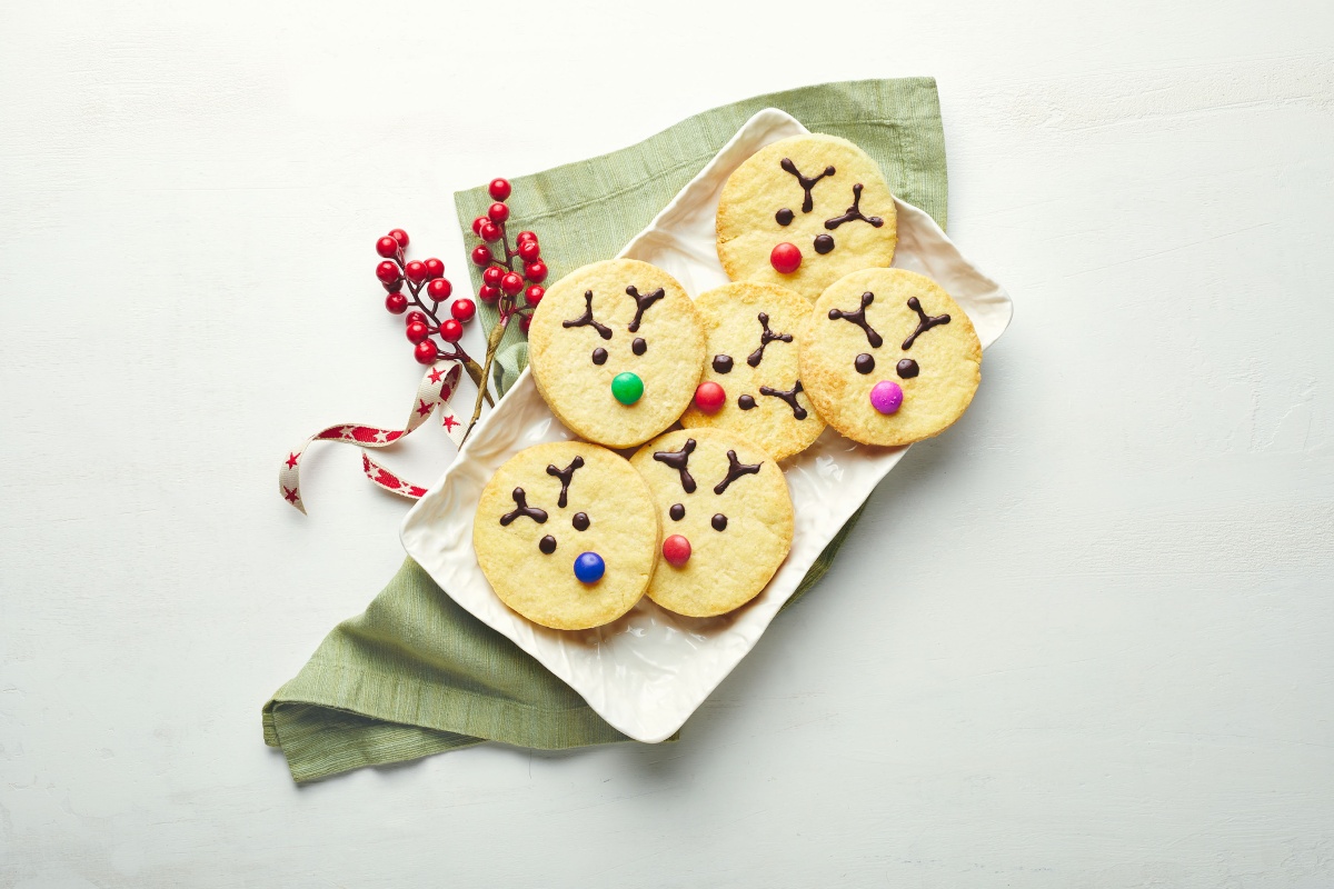 Runde Plätzchen, mit Smarties und Schokolade zu Rentieren verziert, liegen auf einem weißen Teller.