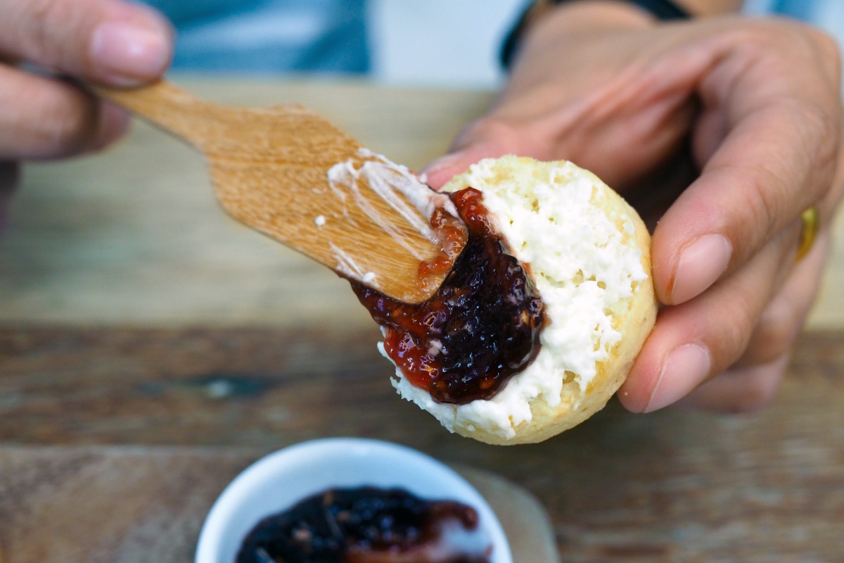 Mit einem Holzmesser wird Marmelade auf einen Scone geschmiert