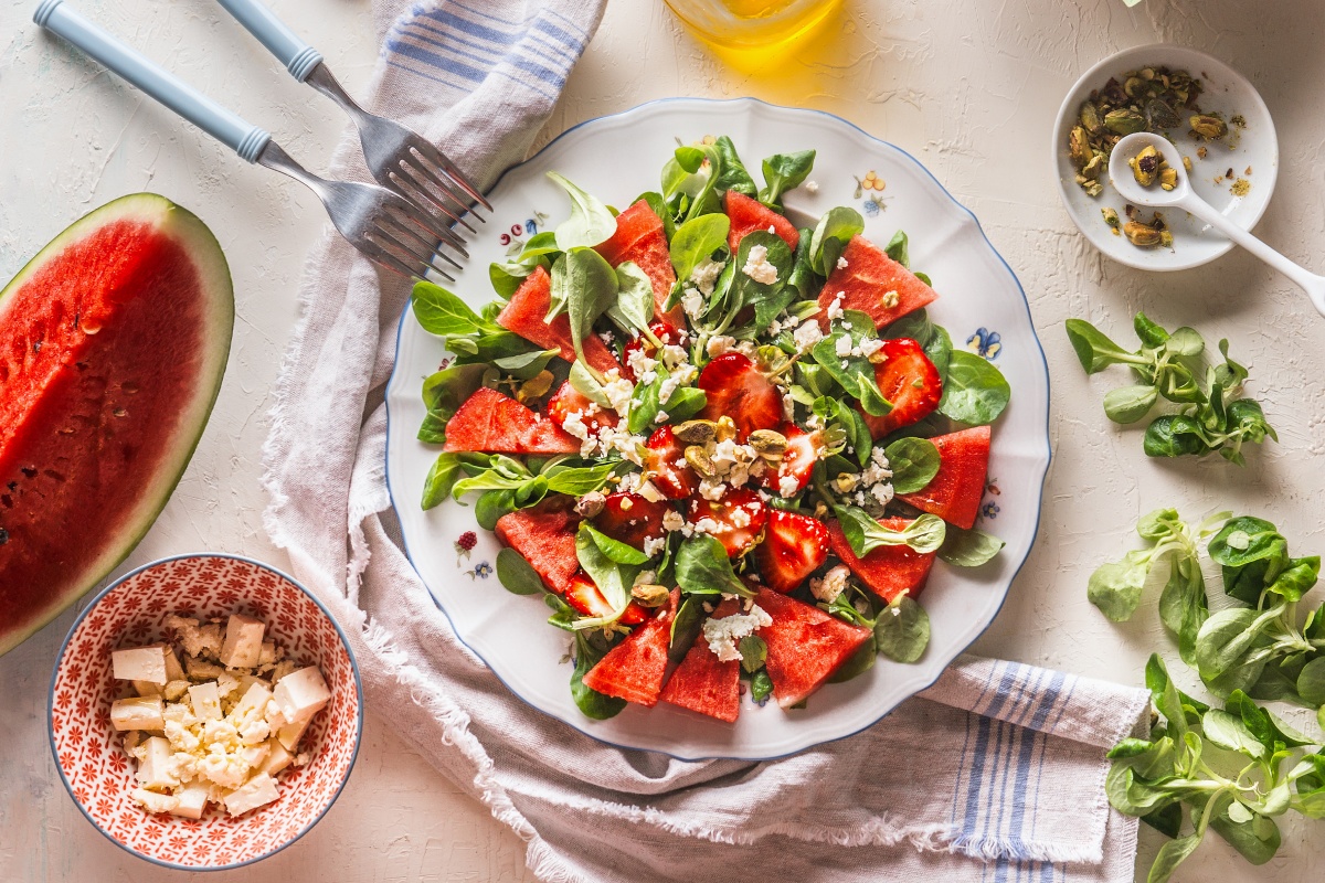 Auf einem gedeckten Tisch steht ein Teller mit einem schön angerichteten Salat aus Wassermelone, Feldsalat, Feta-Käse und Kürbiskernen