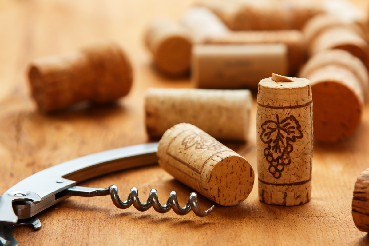 Naturkorken neben einem Korkenzieher auf einer Holzoberfläche.