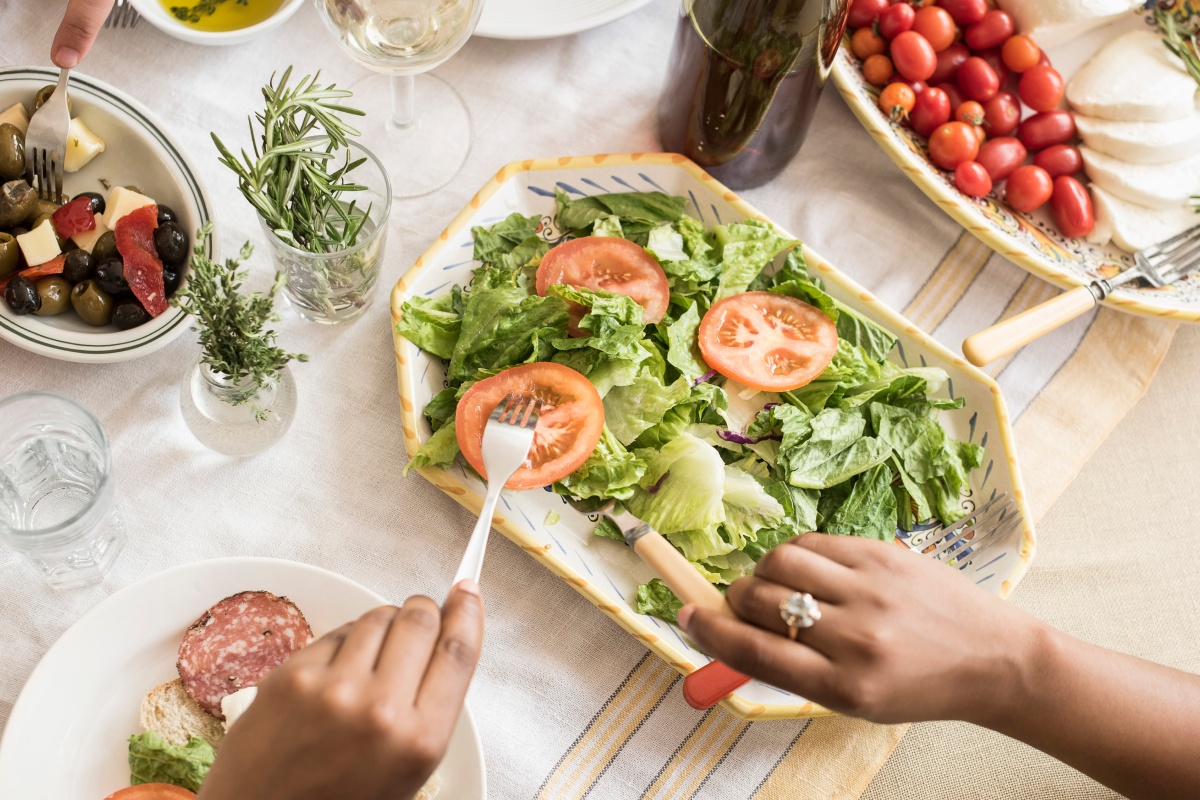 Auf einem Tisch ist ein Salat, sowie Kirschtomaten und etwas Antipasti angerichtet.
