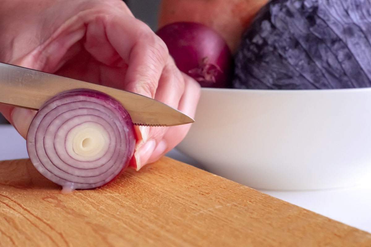 Person schneidet eine rote Zwiebel in feine Ringe auf einem Holzbrett.
