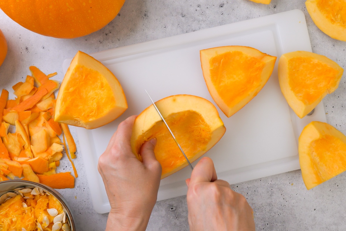 Person schneidet ein großes Stück Kürbis auf einem Schneidebrett, daneben liegen Schalen und Kerne.
