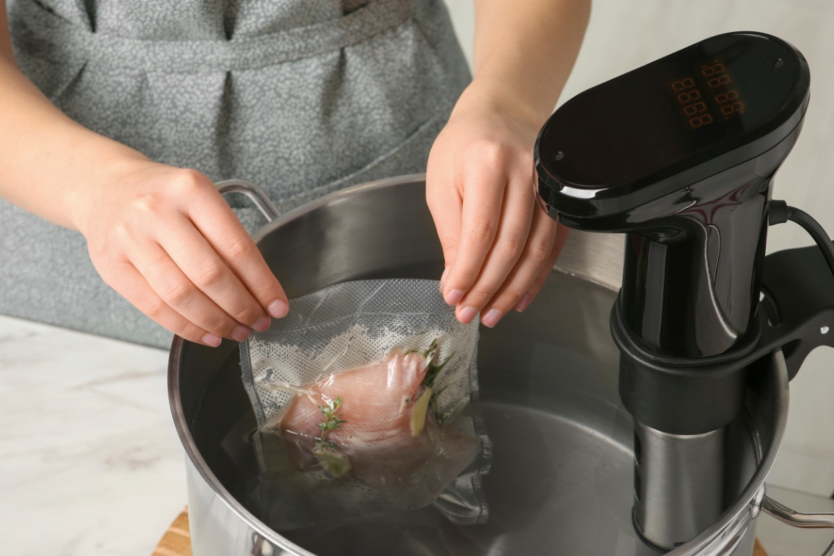 Eine Person gibt vakuumwertes Fleisch in einen, mit Wasser gefüllten, Edelstahltopf.
