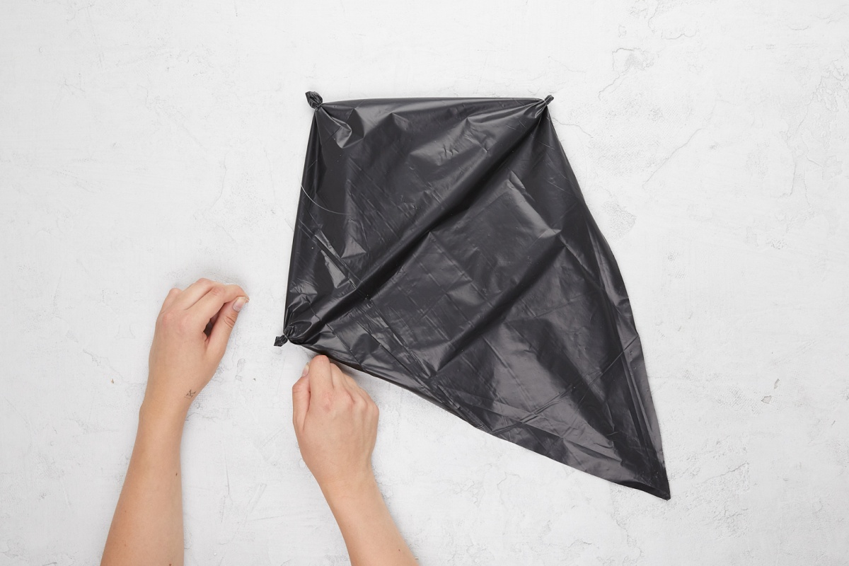 Hände fixieren Mülltüte mit Angelschnur an den Enden der Holzstäbe.