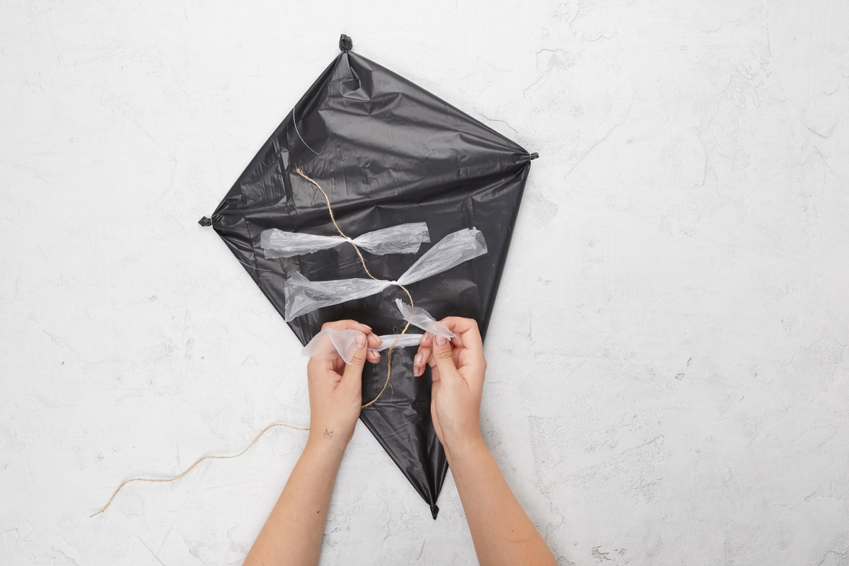 Hände knoten Schleifen aus einer weißer Mülltüte an eine Kordel.