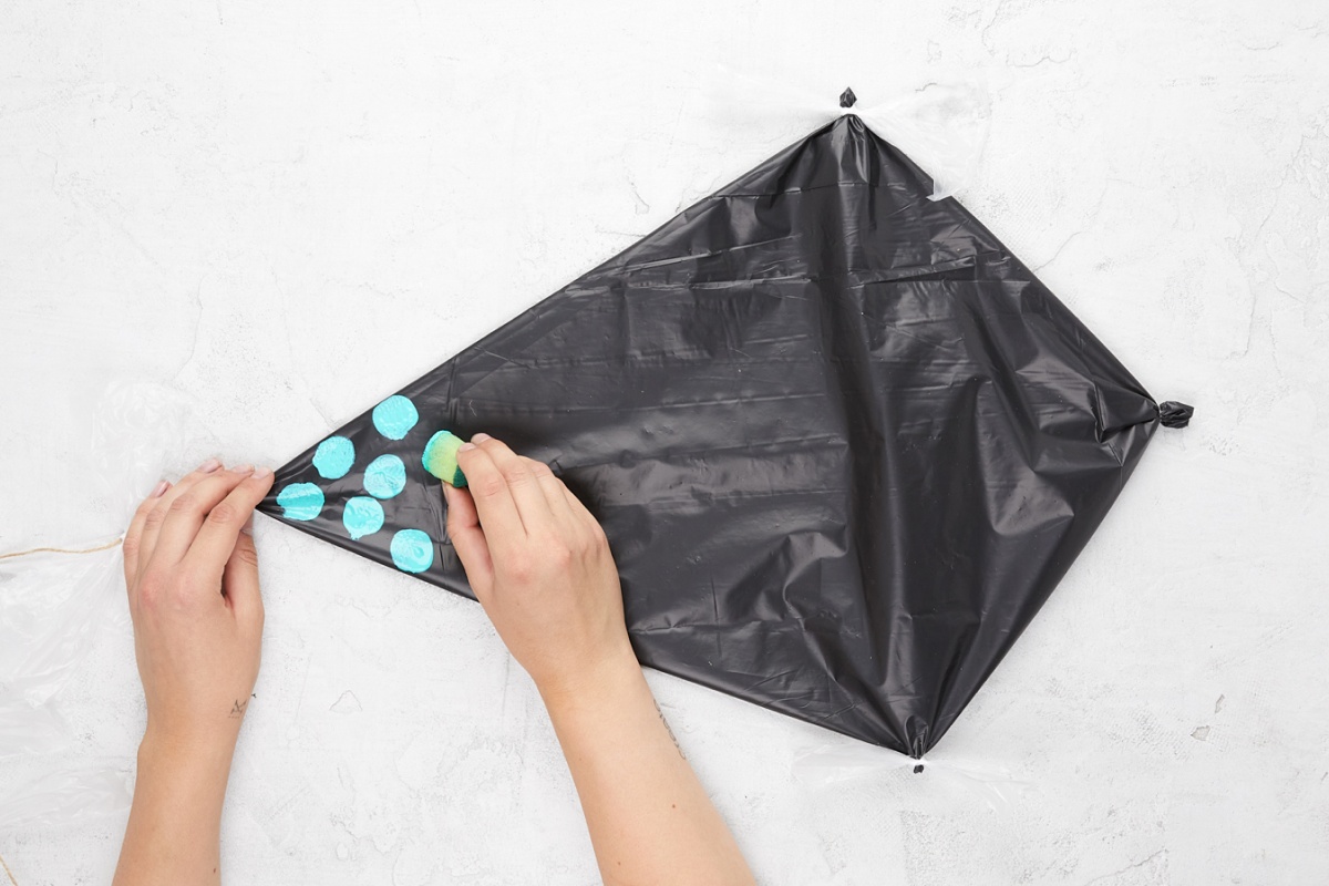 Hände tupfen mit Schwämmchen blaue Kreise auf den Drachen.