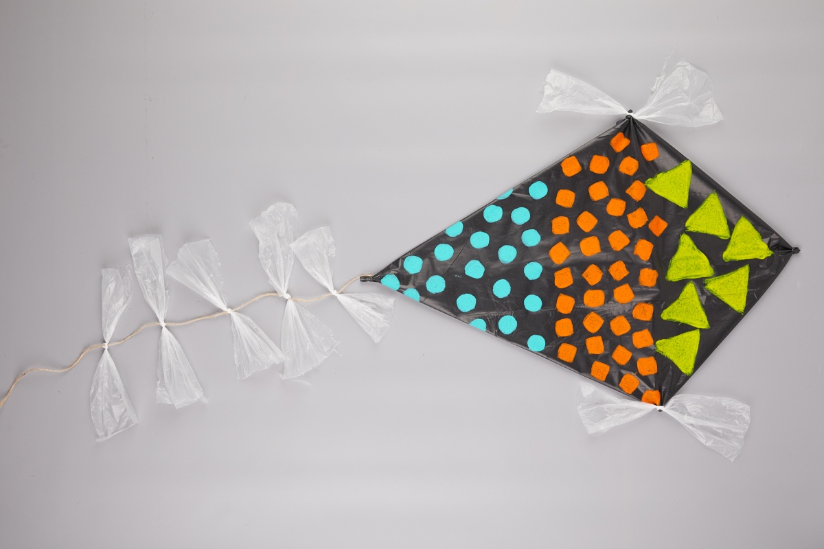 Fertiggestellter selbstgebastelter Drache aus schwarzer Mülltüte mit bunten Mustern dekoriert.