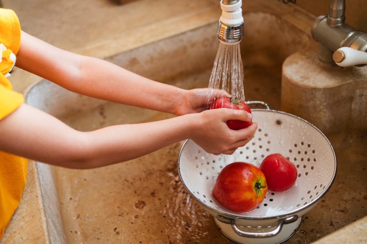 Ein Kind wäscht frische Tomaten in der Spüle ab.